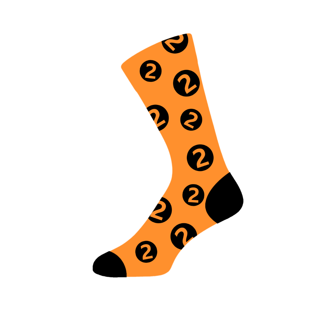 Sure! Here’s a rewritten sentence using the provided product data: A pair of BBC Radio 2 Click & Collect 2026 “Click & Collect BBC Radio 2 in the Park Socks” featuring an orange base with black toes and heels, decorated with black circles each containing an orange number 2 and a curved arrow motif.