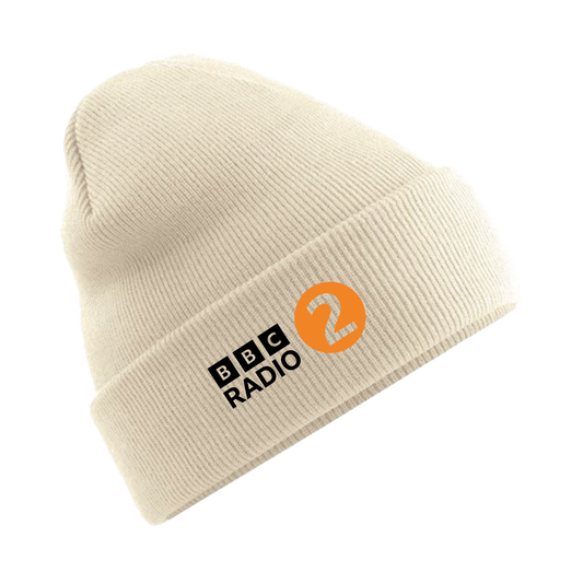 The Radio 2 In The Park Beanie Hat - Sand by 2025 is a cream-colored knit hat with the BBC Radio 2 logo on the front, featuring black text and an orange circle with the number 2 inside.